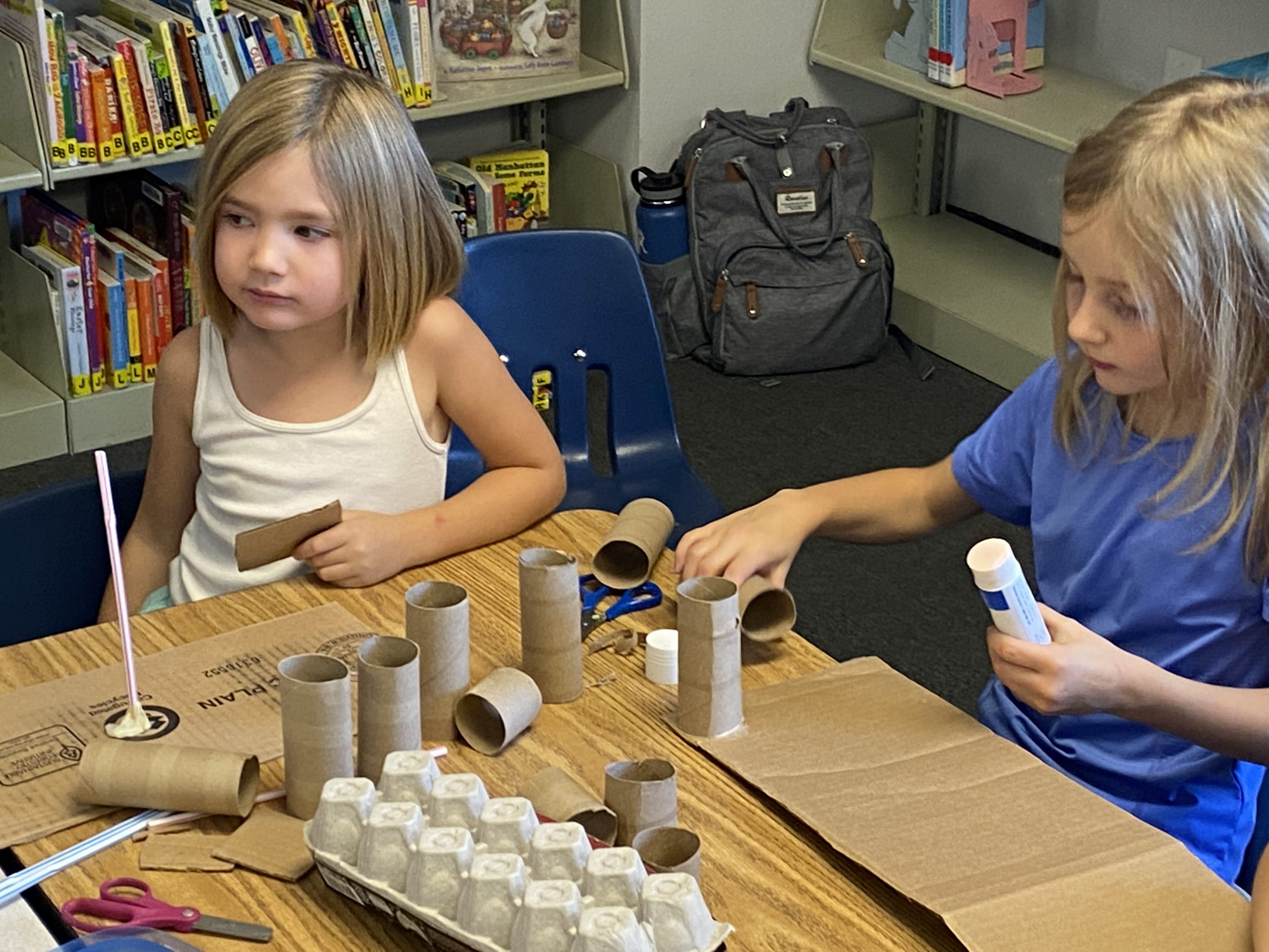 two girls making crafts with toilet paper tubes and cardboard